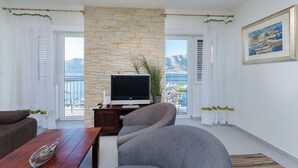 A modern living room with a stone wall, a flat-screen TV, a sofa, and a dining table. - Apartment Jasna By the sea (Baska)
