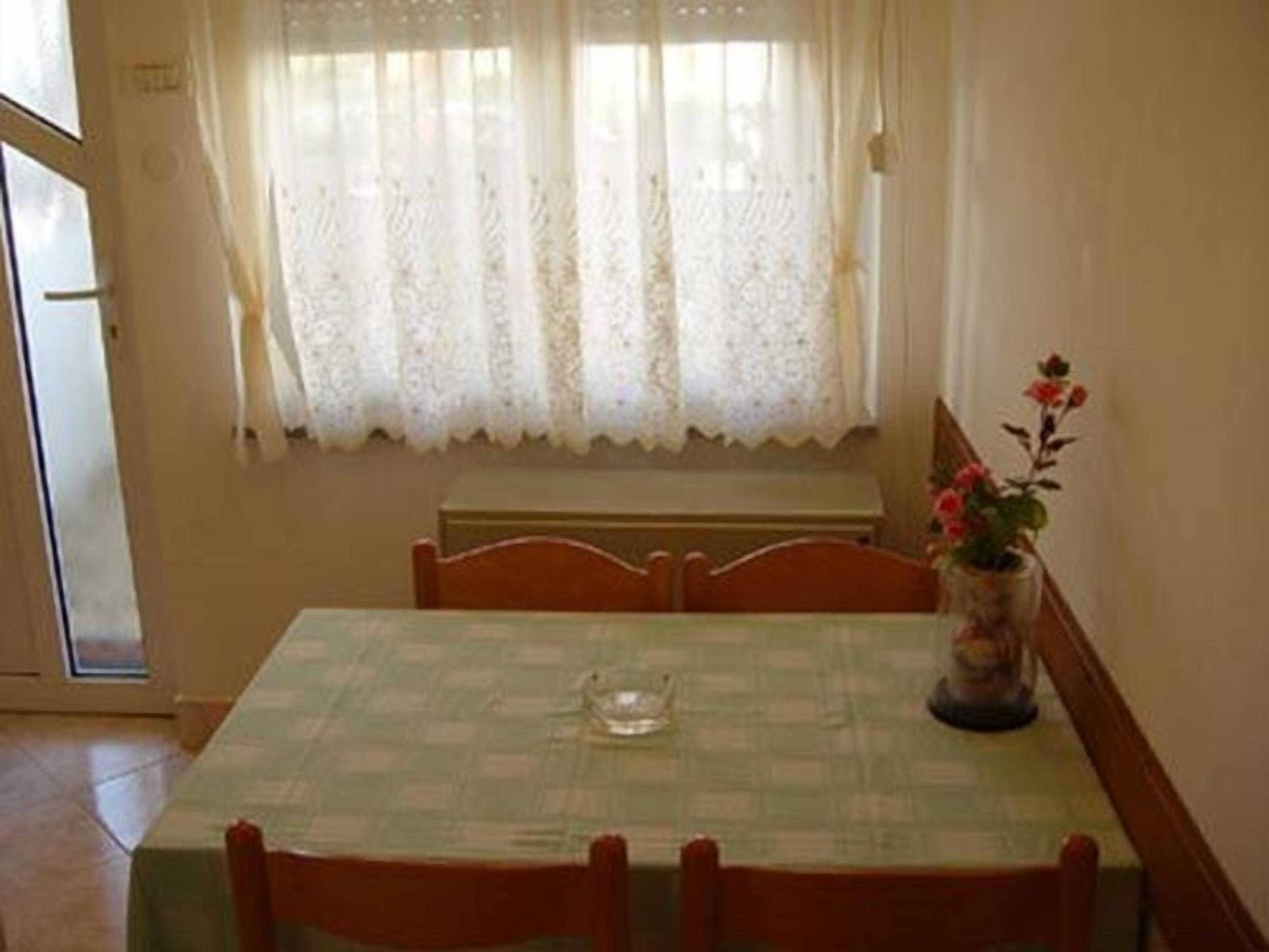 Comedor con una mesa dispuesta para dos, un florero con flores y una ventana con cortinas de encaje.
