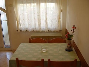 Un coin repas avec une table dressée pour deux personnes, un vase rempli de fleurs et une fenêtre ornée de rideaux en dentelle.