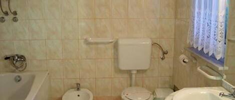 A bathroom with a bathtub, two toilets, a bidet, and a sink.
