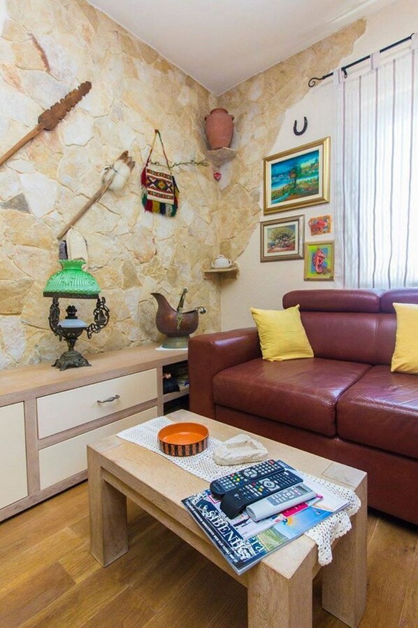 A living room with a stone wall, a red leather sofa, a wooden coffee table, and a small white cabinet. - Apartments Mirella (Tribunj)