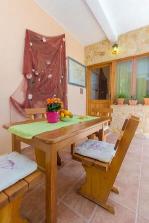 A dining area with a wooden table, chairs, and a pink flower vase. - Apartments Mirella (Tribunj)