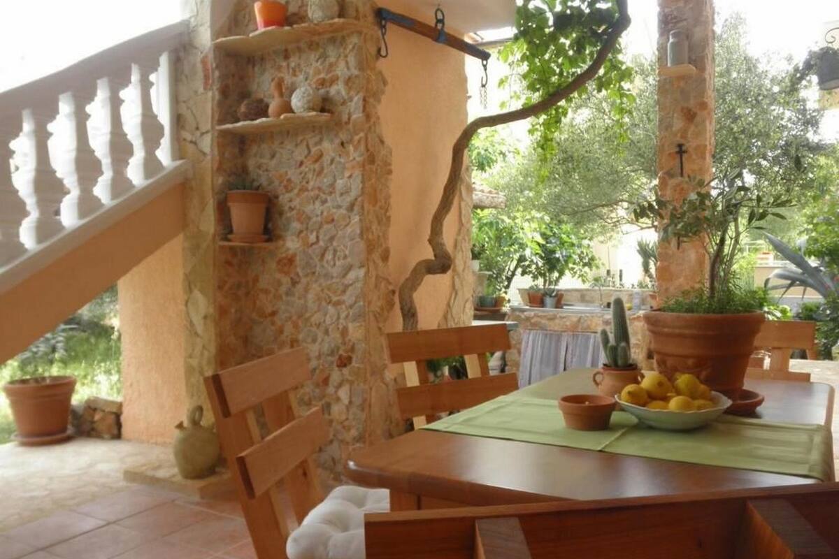 Ένα ξύλινο τραπέζι με καρέκλες, ένας πέτρινος τοίχος και φυτά σε γλάστρες.