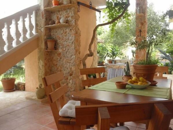 Une table en bois avec des chaises, un mur en pierre et des plantes en pot.