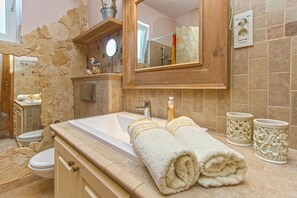 Une salle de bain avec un mur d’accent en pierre, un grand miroir, un lavabo avec deux serviettes et des toilettes.