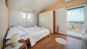 A bedroom with a bed, bedside table, lamp, wardrobe, window, and a view of the city. - Apartments Zinfandel Vodice (Vodice)