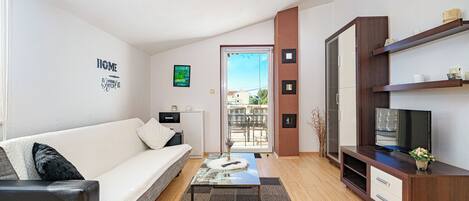 A modern living room with a sofa, coffee table, TV stand, and a view through a glass door.