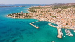 An aerial view of a coastal town with a marina, clear turquoise waters, and a mix of residential and commercial buildings. - Apartments Zinfandel Vodice (Vodice)