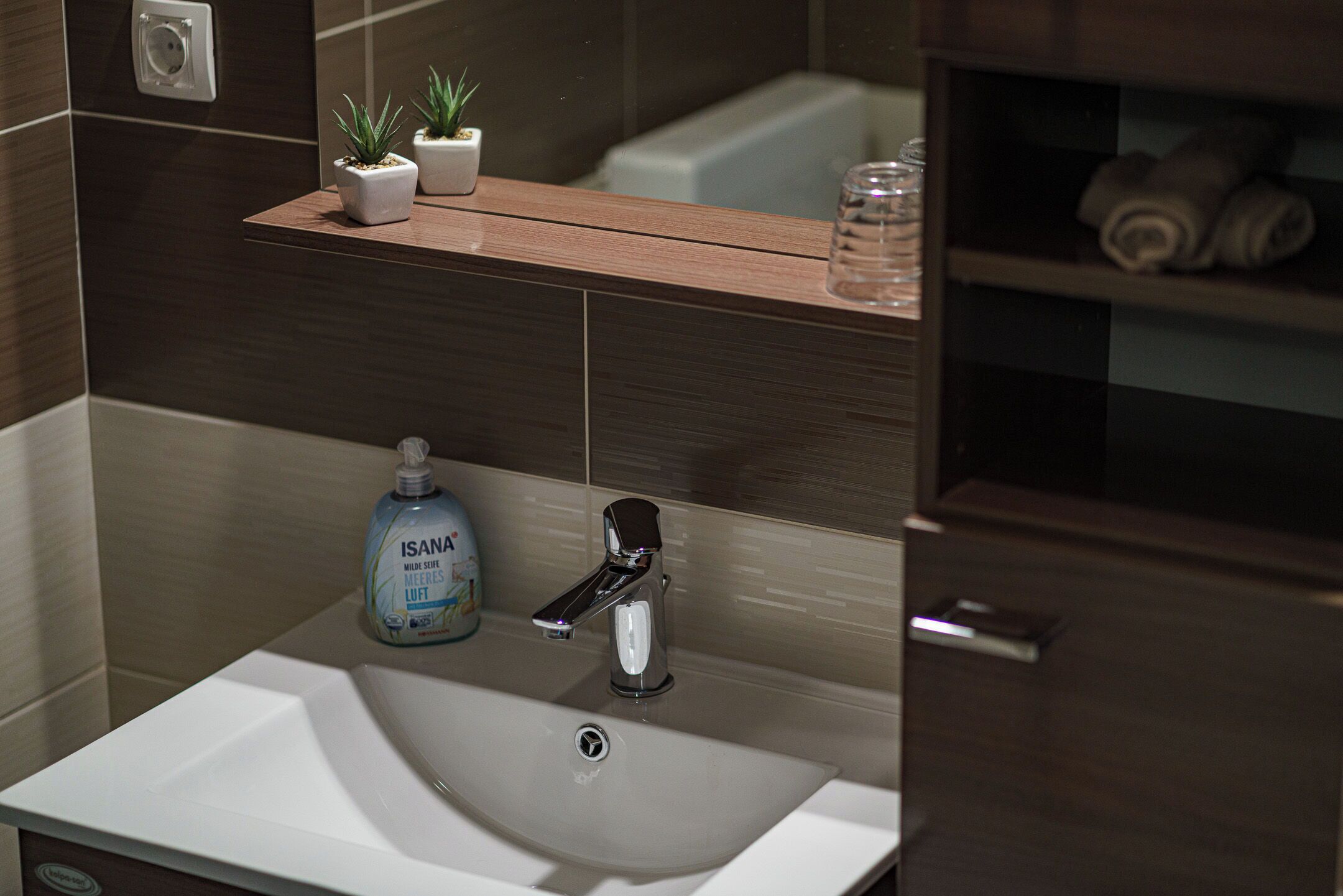 A bathroom with a white sink, a modern faucet, a small potted plant, and a bottle of hand soap.