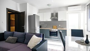 A modern kitchen with white cabinets, a built-in oven, and a dining area with a table and chairs. - Apartments Zinfandel Vodice (Vodice)