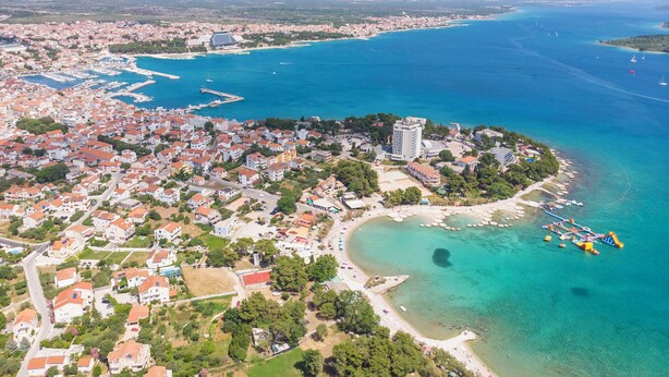 An aerial view of a coastal town with residential buildings, a marina, and a beach with clear blue waters. - Apartments Zinfandel Vodice (Vodice)