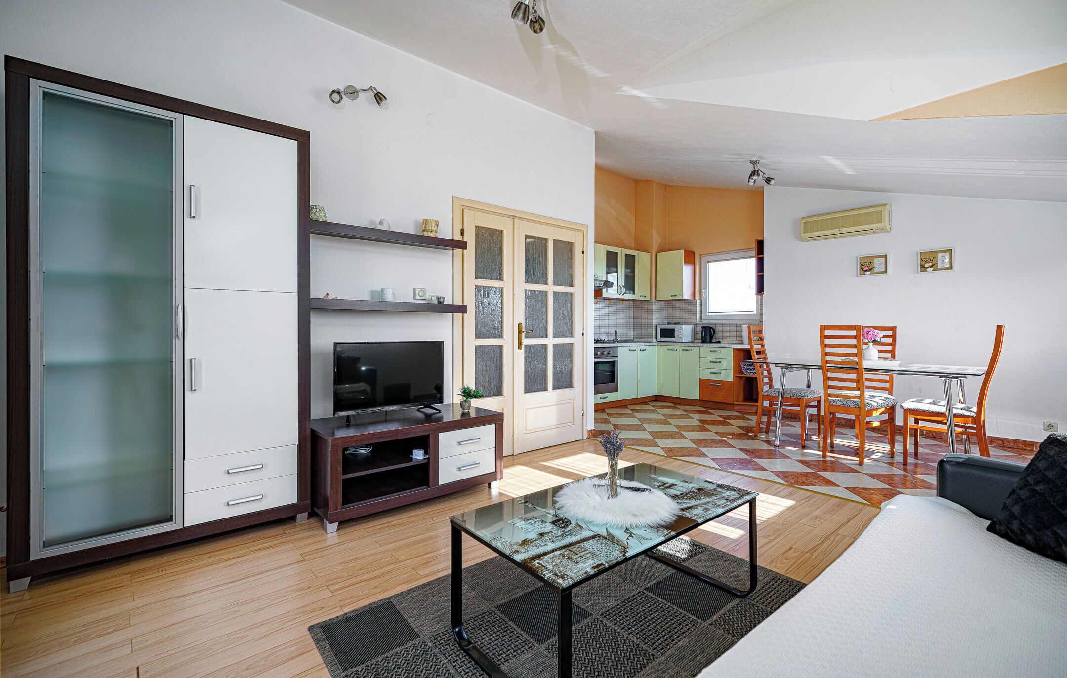 Eine moderne Wohnung mit Wohnzimmer, Essbereich und Küche. Sie verfügt über einen Glastisch, eine Couch und einen Esstisch mit Stühlen.