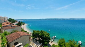 Blick auf die Küste mit Strand, klarem blauen Meer und Gebäuden mit roten Ziegeldächern.