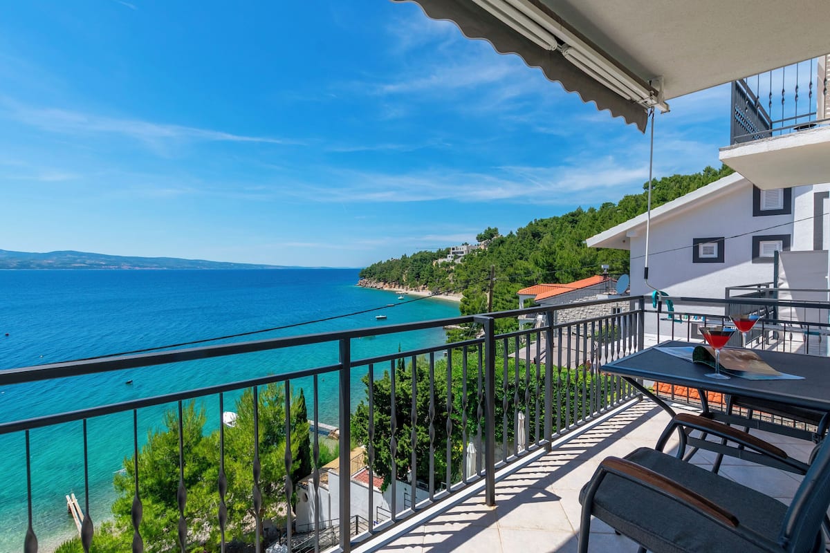 A balcony with a view of the sea, a table with chairs, and a railing.