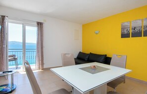 Una camera moderna con tavolo in vetro, due sedie, un divano e un balcone vista mare.