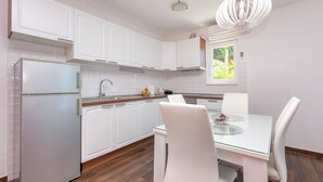 Eine moderne Küche mit weißen Schränken, einem Kühlschrank und einem Essbereich mit einem Glastisch und weißen Stühlen.