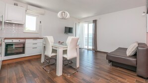 Eine moderne Küche mit weißen Schränken, einem eingebauten Backofen und einem Essbereich mit einem Glastisch und weißen Stühlen.