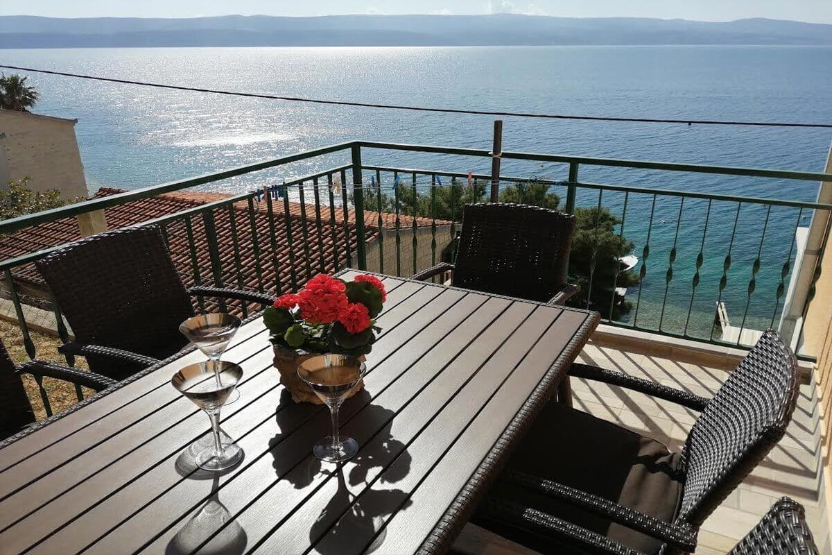 A balcony with a table, two chairs, and a potted plant with red flowers.