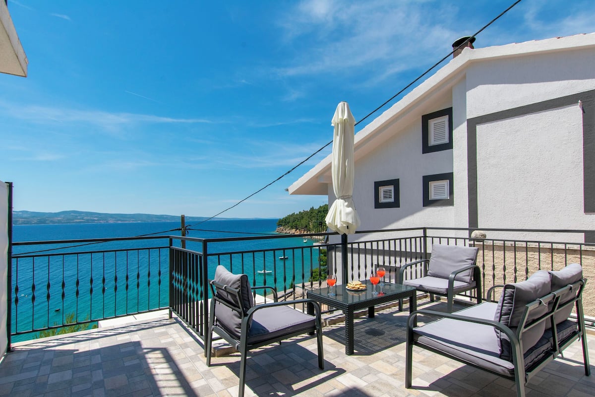 A balcony with a table, chairs, and a view of the sea.