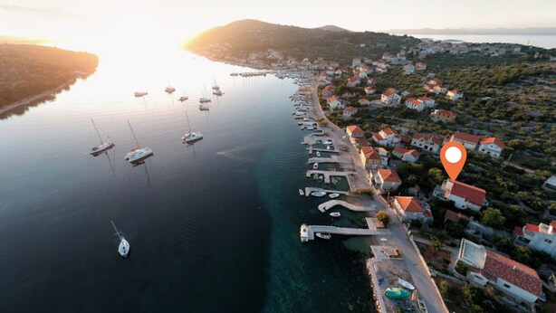 An aerial view of a coastal town with a marina, houses with red roofs, and a clear sky. - Apartment Denis (Sibenik)