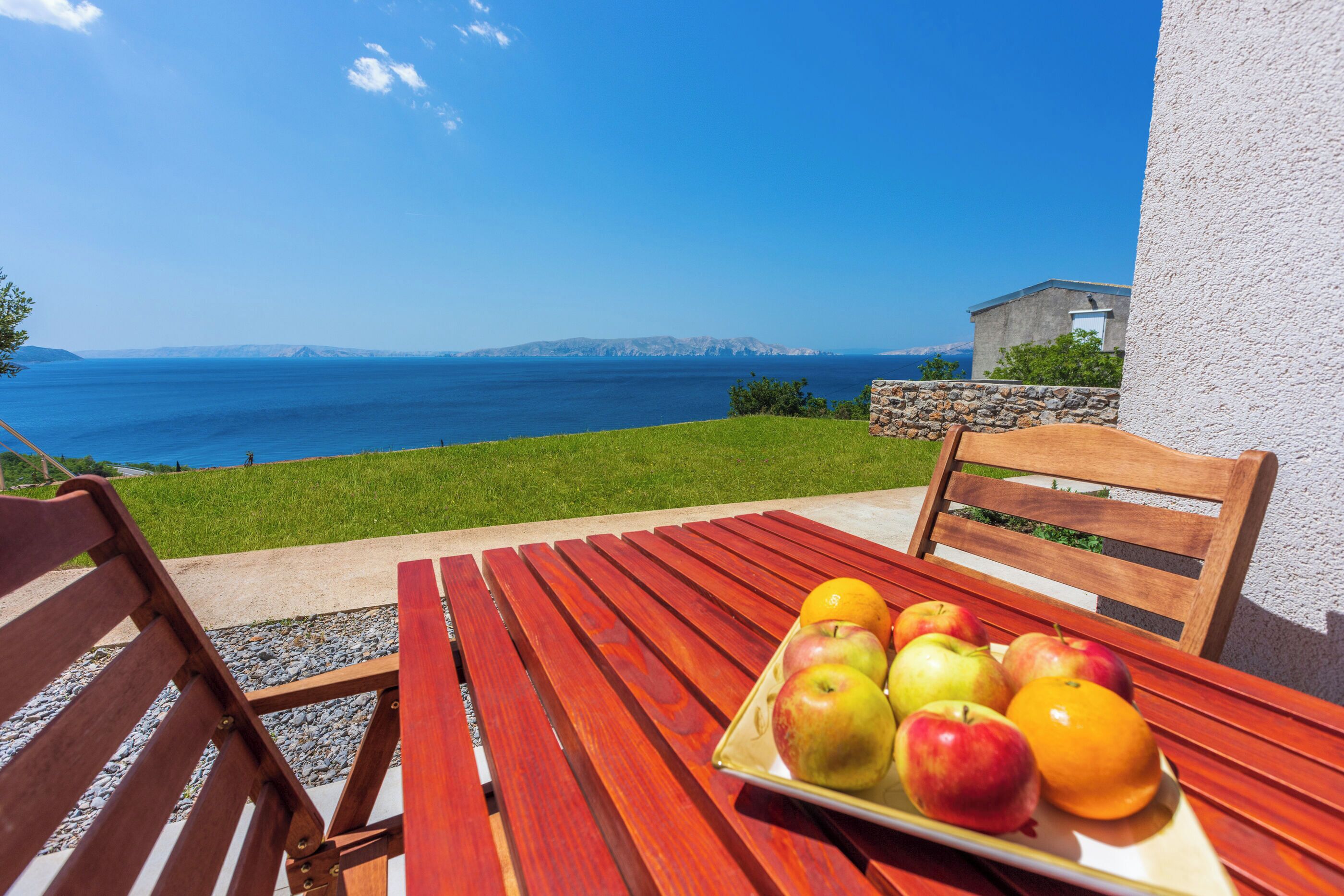 A wooden table with a fruit tray and a bench, overlooking a coastal view.