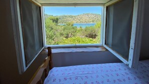 A room with a bed, a window, and a view of a lake and hills. - House Kornati Robinzon (Murter-Kornati)
