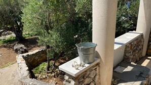 A stone pathway with a metal bucket on a ledge, surrounded by greenery and stone structures. - House Kornati Robinzon (Murter-Kornati)