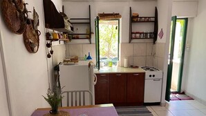 A compact kitchen with a dining table, a refrigerator, a stove, and a window with a view of greenery. - House Kornati Robinzon (Murter-Kornati)