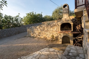 A stone oven built into a wall, surrounded by a gravel area and a stone wall. - Apartments Petra (Solta)