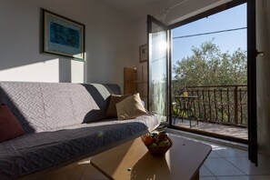 Ett vardagsrum med en soffa, ett soffbord med frukt på, en balkong med ett bord och stolar samt en tavla på väggen.