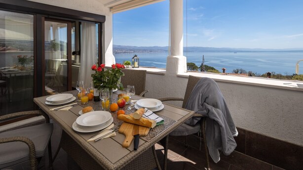 A balcony with a table set for breakfast, overlooking a scenic view of the sea. - Apartment Villa Rebeka (Opatija)