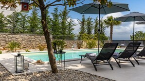 A poolside area with lounge chairs, umbrellas, and a table with bottles and glasses. - Apartment Villa Rebeka (Opatija)