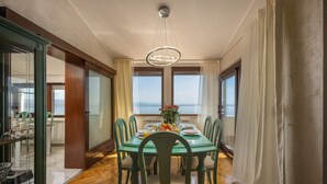 A dining room with a glass table, chairs, and a view of the sea. - Apartment Villa Rebeka (Opatija)