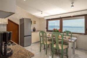 A modern kitchen with a refrigerator, coffee maker, and dining table with chairs. - Apartment Villa Rebeka (Opatija)