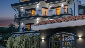 A modern two-story house with a stone facade, a large arched entrance, and a balcony with outdoor lighting. - Apartment Villa Rebeka (Opatija)