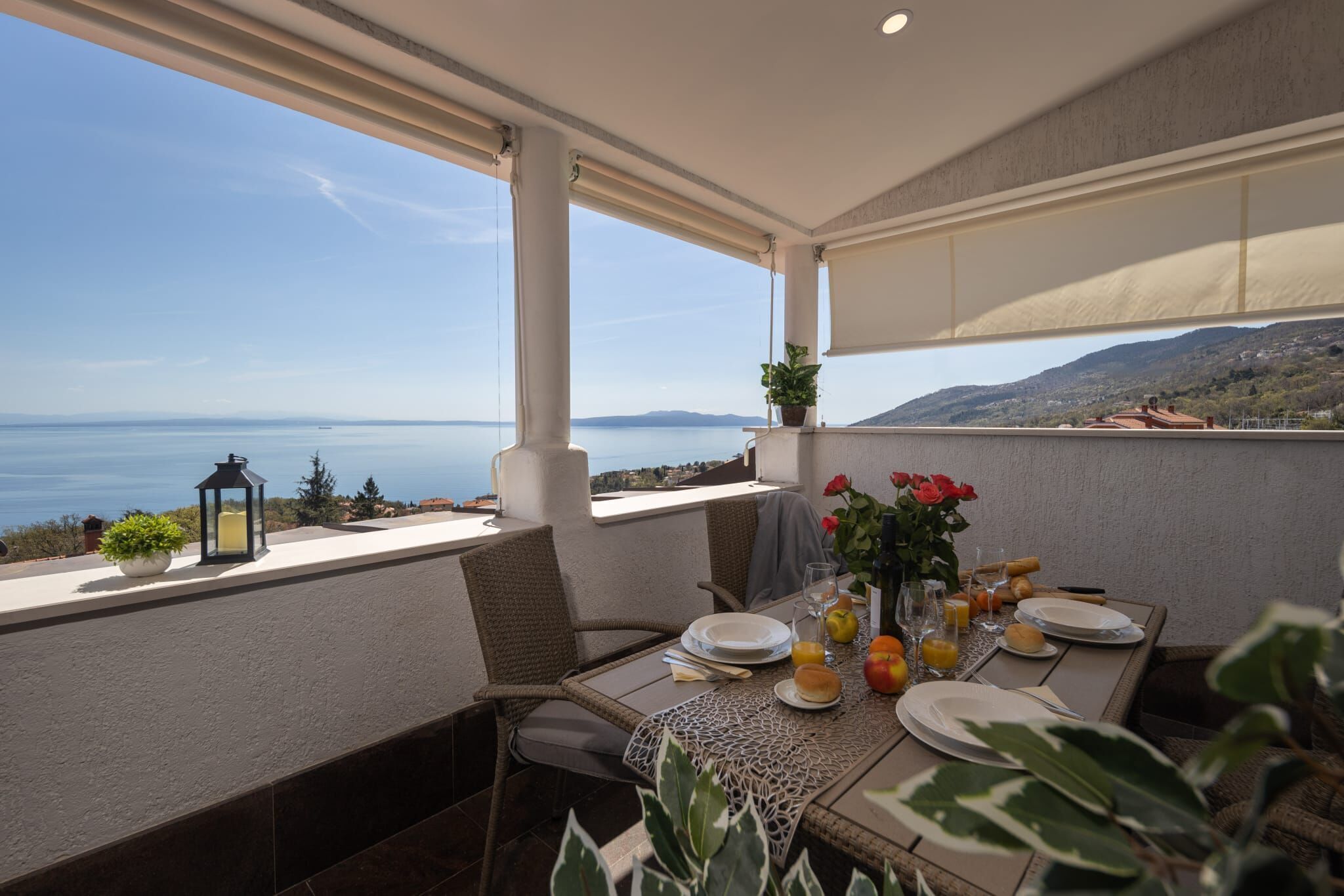A dining area with a table set for two, overlooking a scenic view of the sea and hills.