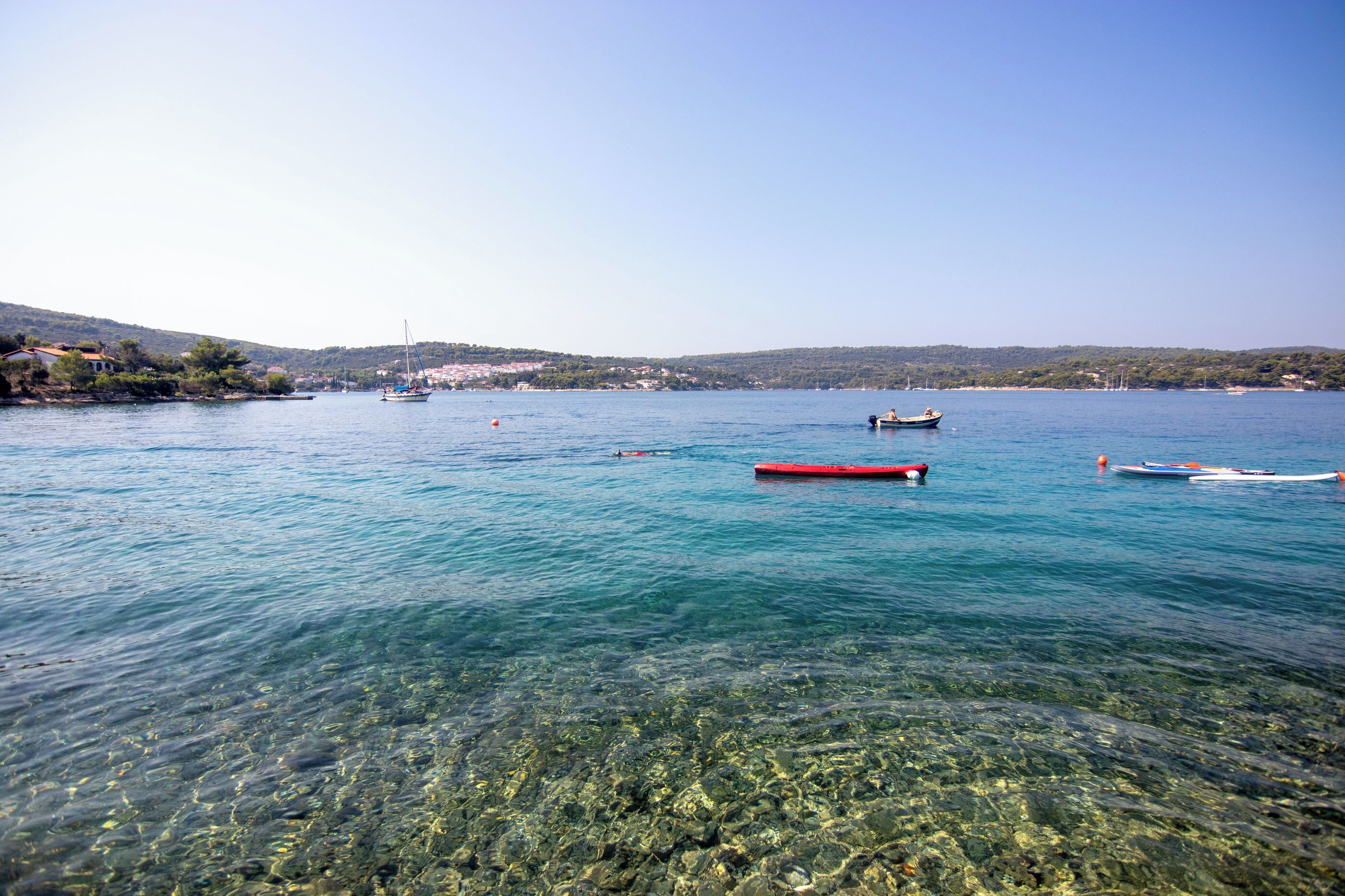 A coastal scene with clear water, boats, and a distant shoreline with buildings.
