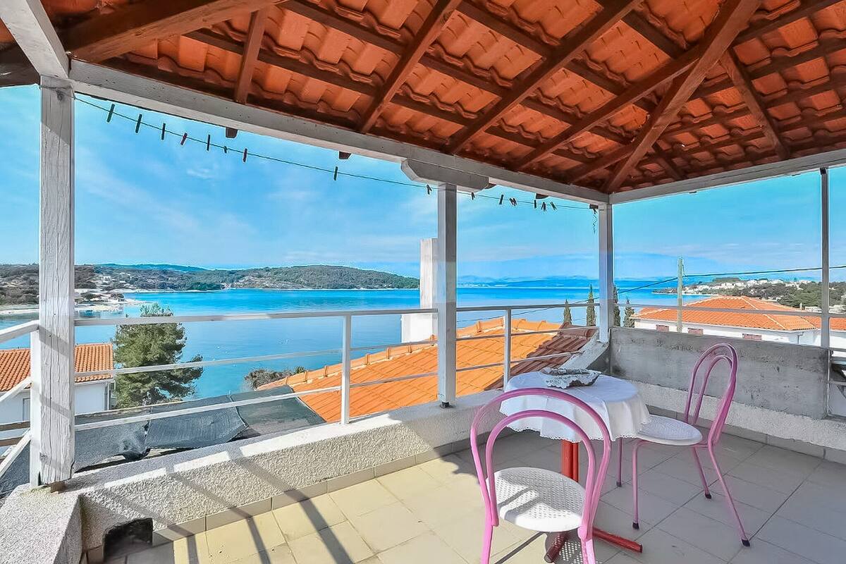 A covered outdoor area with a table and chairs, overlooking a coastal landscape.