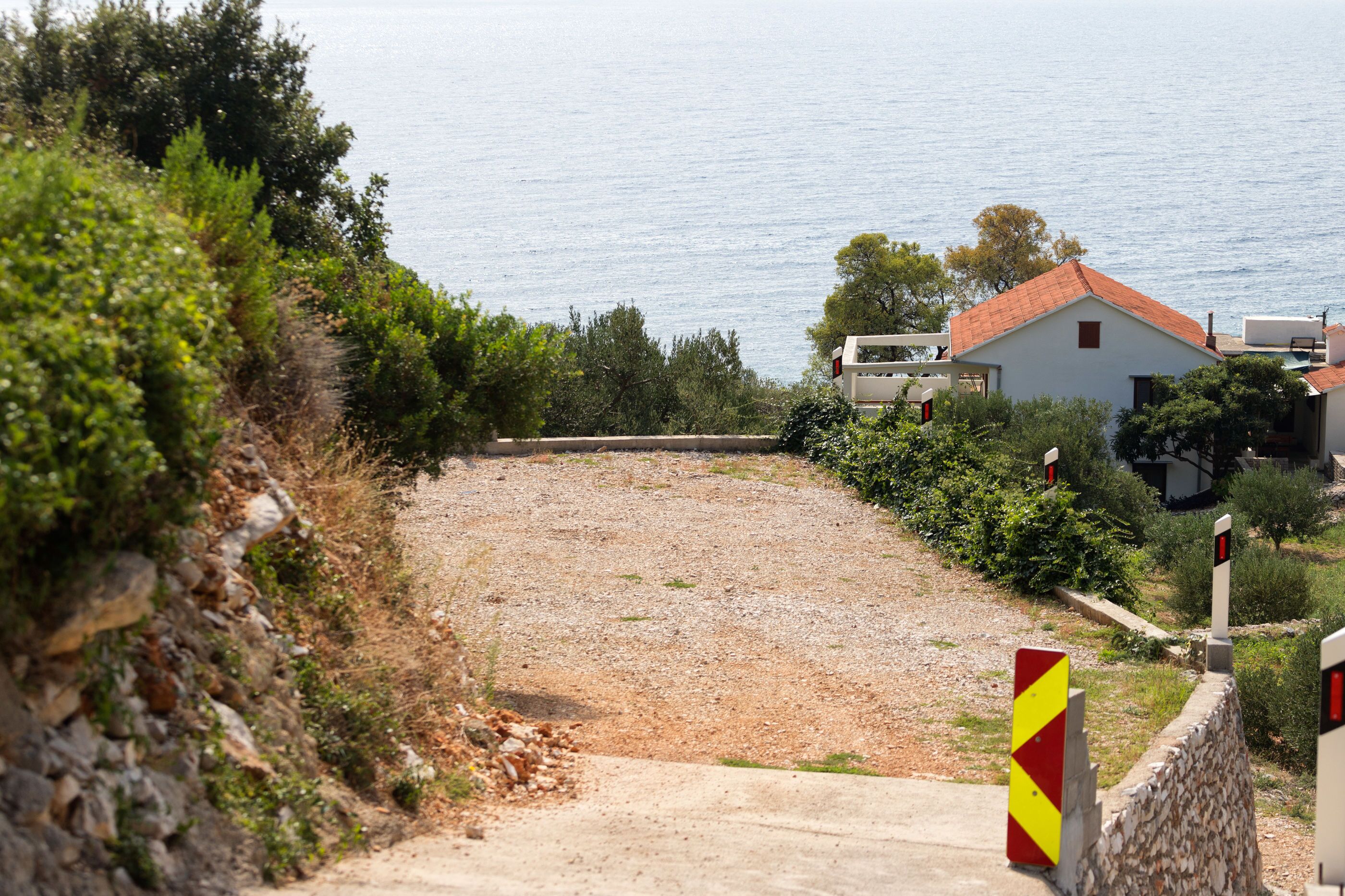 A coastal road with a gravel path leading to a white building with a red roof.