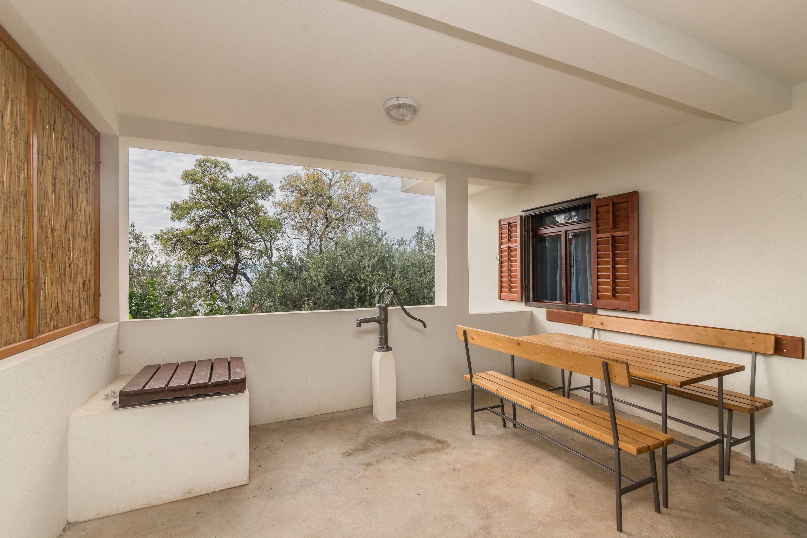 A balcony with a wooden bench, a window with shutters, and a water tap.