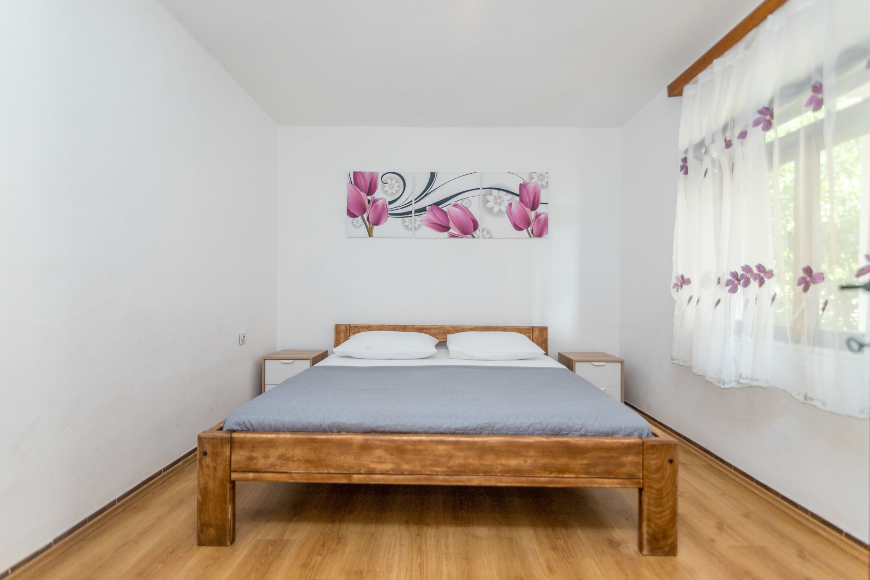 A bedroom with a wooden bed, white walls, and a floral artwork above the bed.