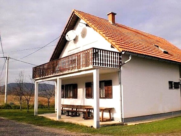 Un bâtiment blanc avec un toit recouvert de tuiles rouges, un balcon et une véranda dotée de bancs.