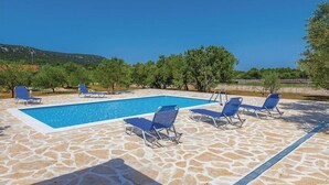 A swimming pool with blue water, surrounded by stone tiles and blue lounge chairs. - House Hacienda (Tisno)