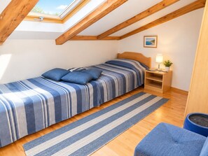 Ein Schlafzimmer mit Dachfenster, einem Bett mit gestreifter Bettwäsche, einem Nachttisch mit Lampe und einer kleinen Pflanze.