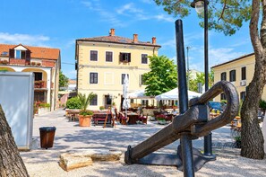 Une place carrée dotée d’un espace extérieur aménagé avec des sièges, une grande sculpture servant de point central et des bâtiments aux toits recouverts de tuiles rouges.