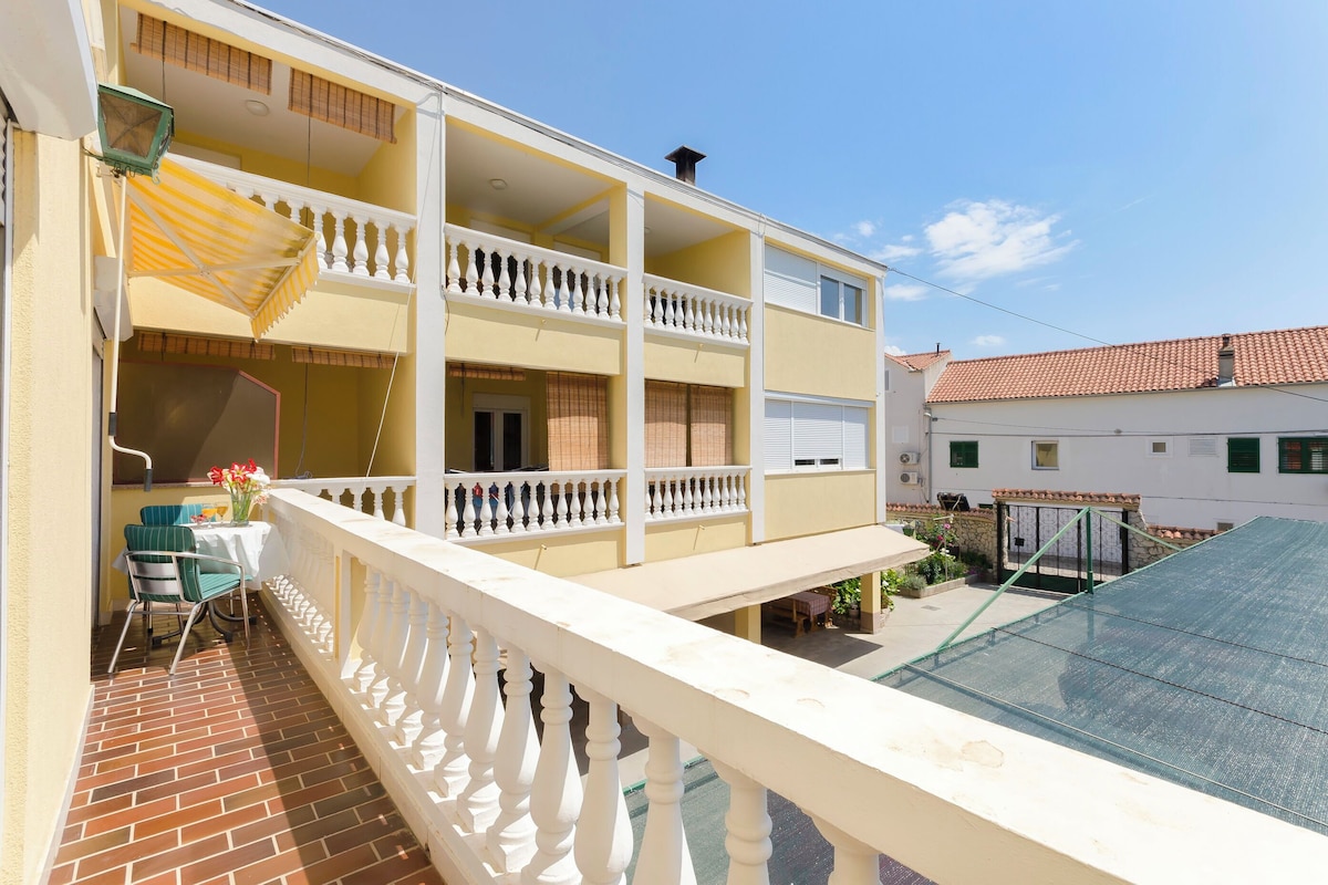 A two-story building with balconies, a patio with a table and chairs, and a glass roof.