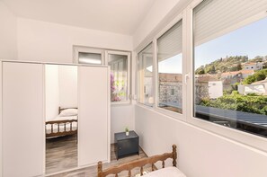 A bedroom with a bed, a wardrobe, a small table, and a window with a view of a hillside. - Apartments and Room Lotus (Tribunj)