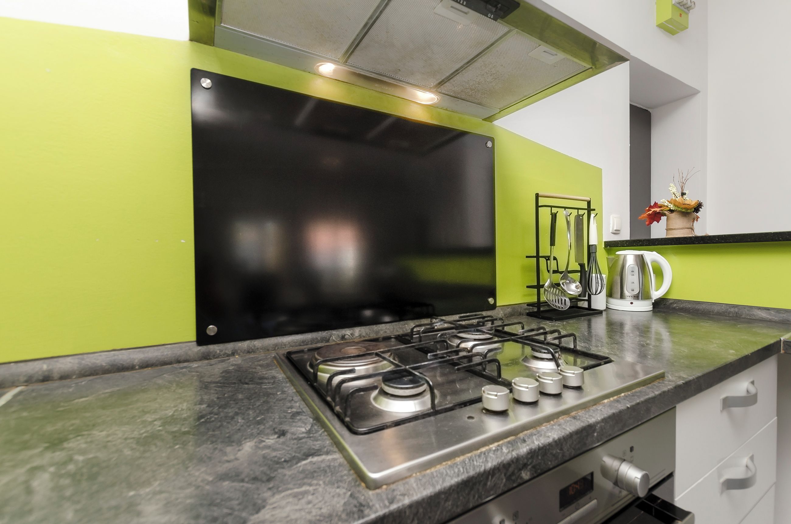 A kitchen with a gas stove, a kettle, and a coffee maker on the counter.