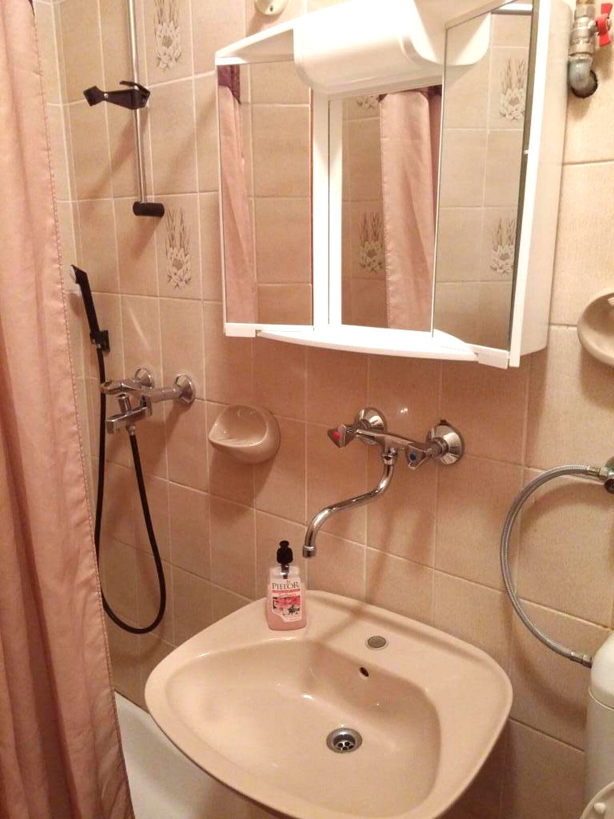 Een badkamer met een wastafel, spiegel, douche en handdoekhouder.