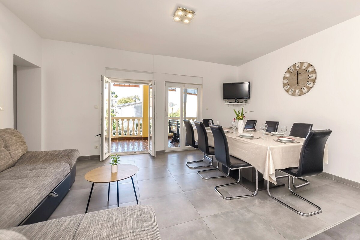 A modern living room with a sofa, a small round table, and a dining area with a table set for six.